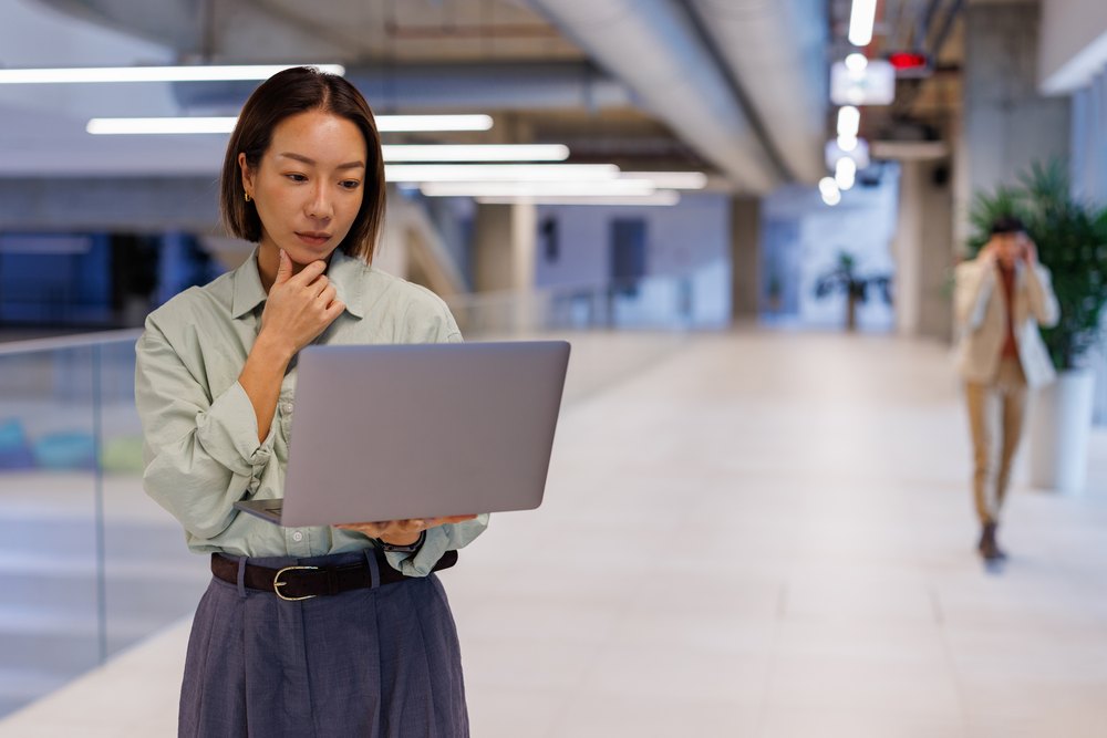 Businesswoman pausing thoughtfully over a laptop in an office walkway, representing comparing Philippines staffing partners